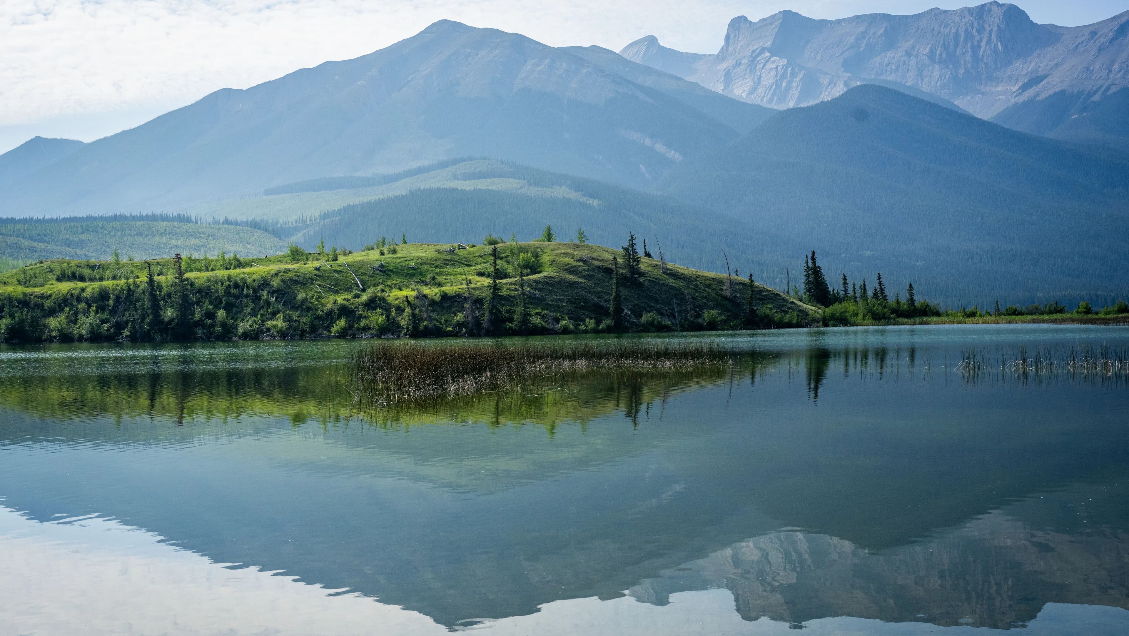 A calm lake mirrors the mountains and forest of Jasper National Park, the setting for Ashley Paulson's Bike the Rockies cycling series.